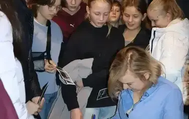 Angelika składa autografy na zakładkach, dzieci stoją wok&oacute;ł niej