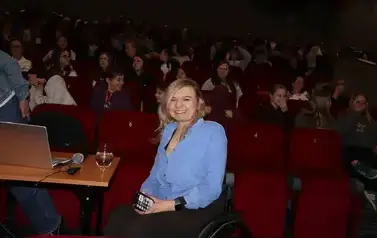Angelika Chrapkiewicz-Gądek pozuje do zdjęcia, uśmiecha się, w tle publiczność czyli dzieci ze szkoły