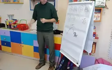 Łukasz Zabdyr stoi przed tablicą na kt&oacute;rej narysował r&oacute;żne oznaki niepełnosprawności