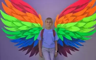 Jenda z uczestniczek pozuje na tle kolorowych skrzydeł