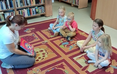 dzieci siedzą na dywanie i słuchają bajki