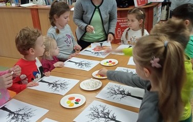 Dzieci wykonują pracę plastyczną przy stolikach