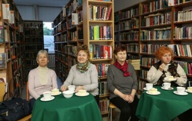 czytelniczki siedzą przy stołach słuchają i piją kawę