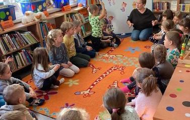 Dzieci siedzą na dywanie i słuchają bibliotekarki 